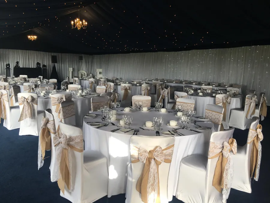 White stretch chair covers with hessian and lace sashes around dinner tables in a marquee