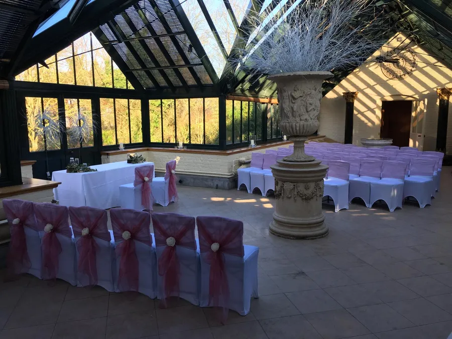White stretch chair covers with dusky-pink organza hoods and ivory roses in a glass conservatory