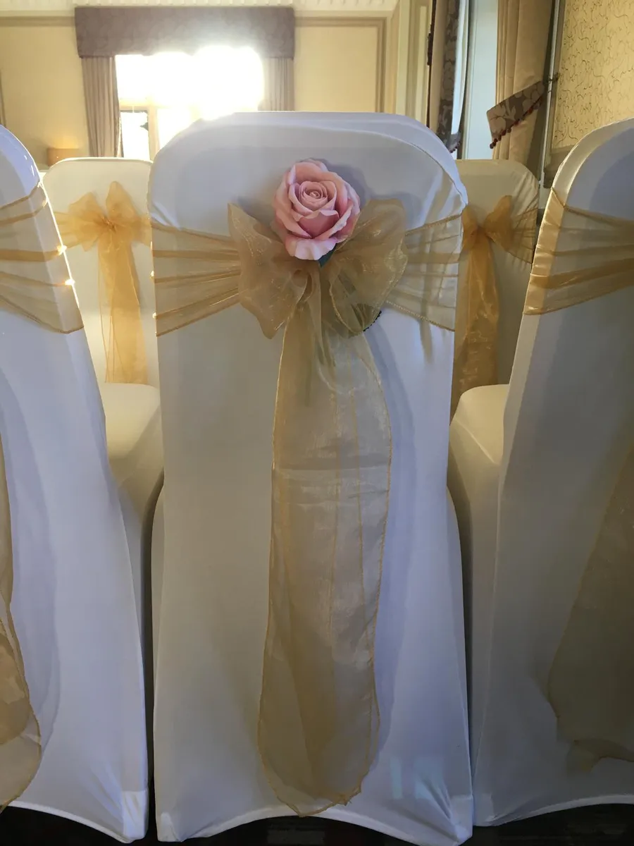 Close-up of a white stretch chair cover with a gold organza bow and a blush rose